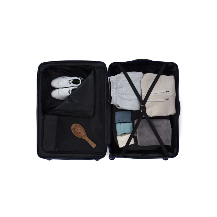 The Reebok Action Duo 2 Piece Luggage Set, featuring spinner wheels, opens to reveal neatly packed clothes, white sneakers, a wooden hairbrush, and folded garments secured with elastic cross-straps—organized and ready for travel.