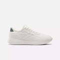 The Reebok Active Lite Shoes are white minimalist sneakers with a low profile, white laces, a textured sole, green heel accent, and a breathable upper for all-day comfort. Shown on a plain white background.