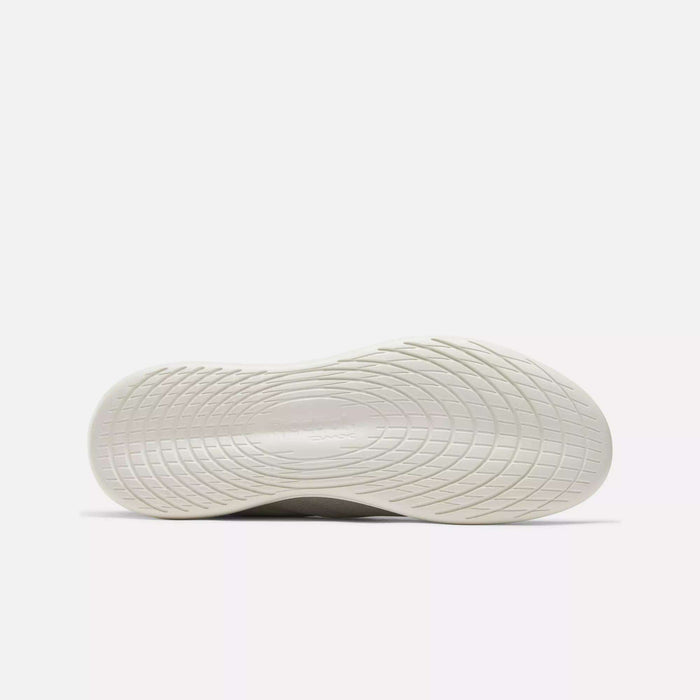 The image displays the bottom view of a white Reebok Active Lite Shoe sole featuring textured wavy and circular treads on a plain white background, emphasizing the minimalist sneaker’s stylish and comfortable design.