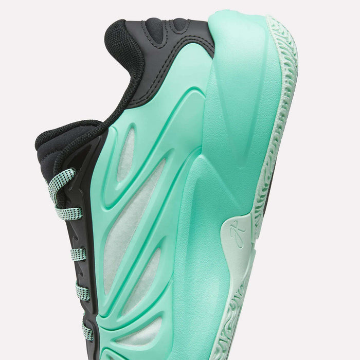 A close-up of the Reebok Angel Reese 1 Basketball Shoes for Big Kids, featuring a teal sole and side details, a white midsection, and black upper accents, displayed against a white background.