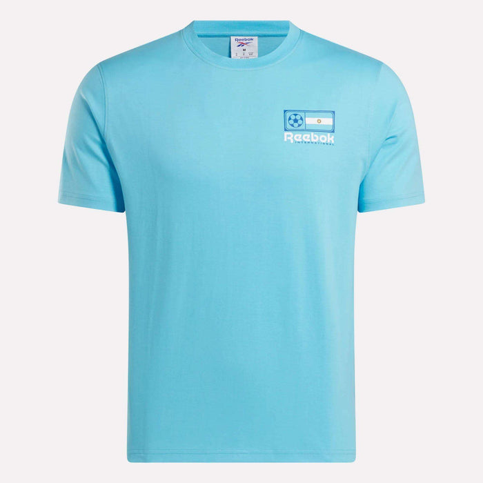 The Reebok Argentina Football T-Shirt is a light blue cotton tee with a small left chest logo featuring the Argentina flag, soccer ball, and "Reebok" in white—a great choice for Argentina fans.