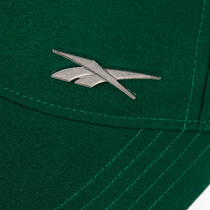 Close-up of the Reebok Badge Cap in green, featuring a silver Reebok logo emblem near the stitching and a Speedwick sweatband for moisture-wicking comfort.
