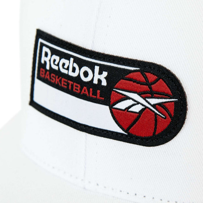 Close-up of the Reebok Basketball Trucker Cap, a white snapback hat with a rectangular patch displaying the Reebok logo, "BASKETBALL" in red, and a red basketball graphic—perfect for basketball fans.