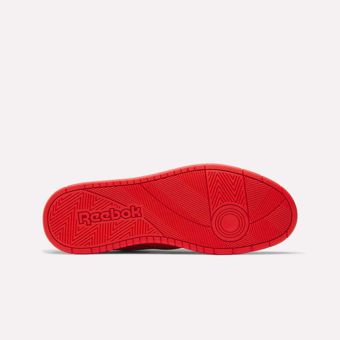 The image displays the vibrant red rubber sole of Reebok's BB 1000 Retro Basketball Shoes, showcasing the iconic Reebok logo and a geometric tread pattern with linear and circular details. Set against a plain light gray background, the sole evokes a nostalgic court style inspired by vintage sneakers.