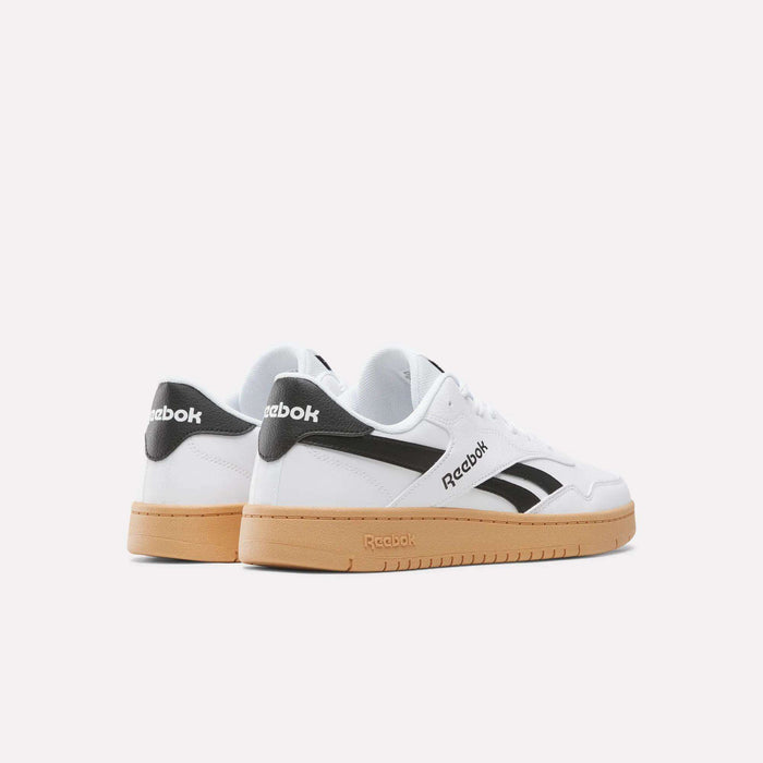 A pair of BB 1000 Shoes by Reebok featuring a white leather upper, black accents, and gum soles, photographed from a rear side angle against a plain light background—a classic design inspired by ’80s heritage.