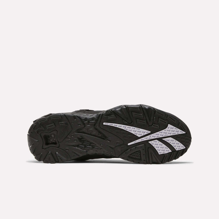 The image shows the black rubber outsole of the Reebok Brutus Low Shoes, featuring textured treads, white angular accents, and grooves for traction, blending classic heritage style with modern street-ready design.