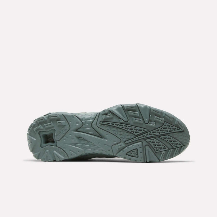 The image shows the textured outsole of Reebok Brutus Low Shoes in a muted green, displaying geometric patterns for traction and grip. The background is plain white.