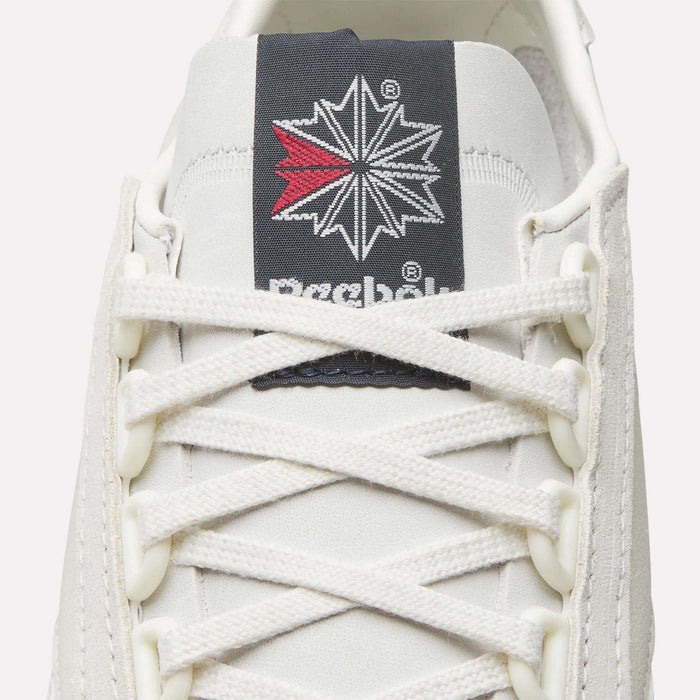 Close-up of Reebok Camargue Shoes in white, showcasing white laces, a tongue label with the Reebok logo, and a red and black star—a luxury leather archive trainer for sneaker fans.
