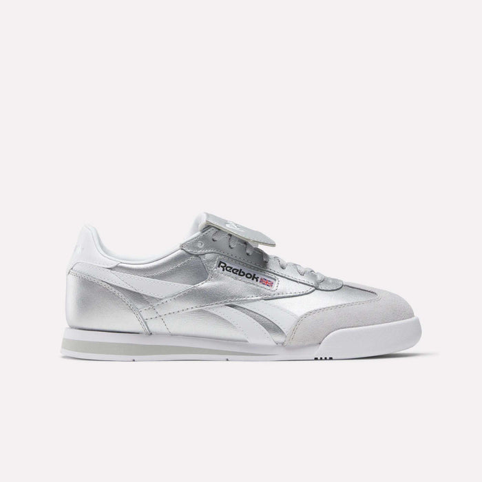 A pair of Reebok Campio XT Kilty Shoes featuring silver color, white and gray accents, tennis-inspired low-top design, and the Reebok logo on the side, showcased against a plain white background.