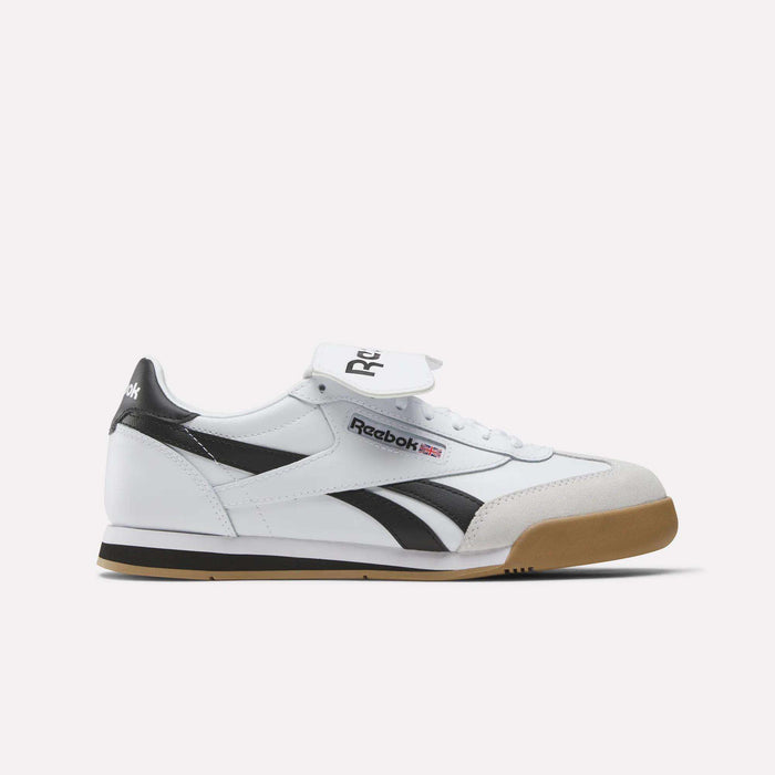 The Campio XT Kilty Shoes by Reebok feature a white and black leather upper, gum sole, tennis-inspired style, black Reebok logo, and Union Jack flag detail on the side. Shown against a plain white background.