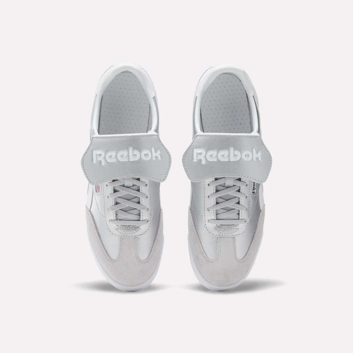 A pair of Reebok Campio XT Kilty Shoes in white leather are shown from above, side by side on a plain white background. They feature laces, wide velcro straps across the top, and the Reebok logo in white text.