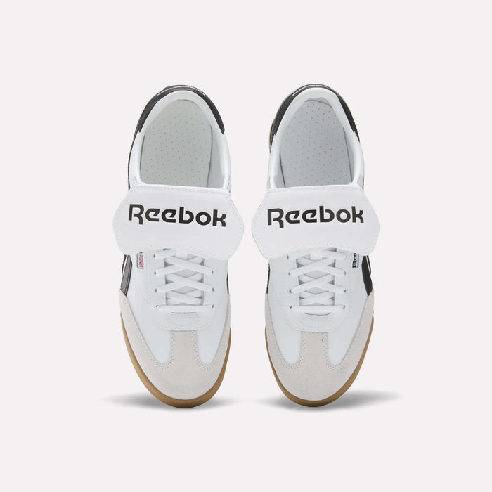 The Reebok Campio XT Kilty Shoes feature a tennis-inspired style with white uppers, beige suede toe caps, brown gum soles, black accents, and large white velcro straps with the bold black Reebok logo.