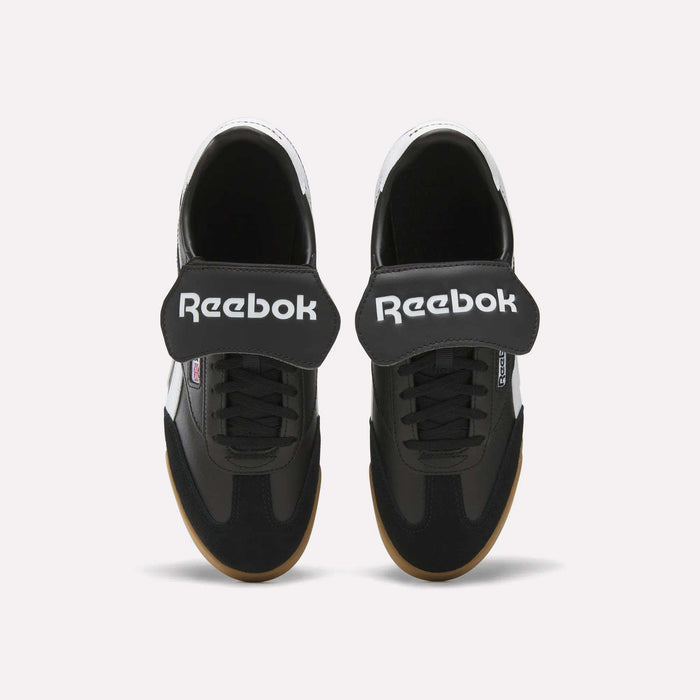 Top view of Reebok Campio XT Kilty Shoes in black with wide Velcro straps, white Reebok logo, black laces, and light brown soles. These tennis-inspired sneakers are shown on a plain white background.