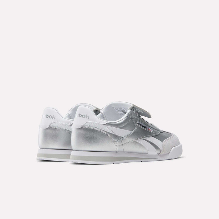 A pair of Reebok Campio XT Kilty Shoes in silver and white, shown from the back and side, with the Reebok logo visible on the heel and side. These tennis-inspired sneakers are displayed against a plain white background.