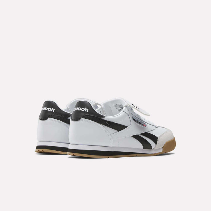The Reebok Campio XT Kilty Shoes, in white with black accents and gum soles, showcase classic tennis-inspired style. Viewed from the back and side on a plain light background, the Reebok logo is visible on each heel and side.