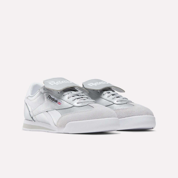 A pair of Reebok Campio XT Kilty Shoes in light grey and white, with a classic tennis-inspired style, Velcro straps over the laces, and the Reebok logo on the side and tongue, shown on a plain white background.