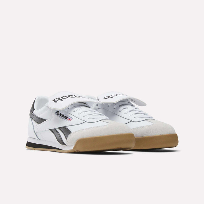 A pair of Reebok Campio XT Kilty Shoes in white with black accents, gum soles, and large white Velcro straps featuring the black Reebok logo are placed side by side on a plain white background.