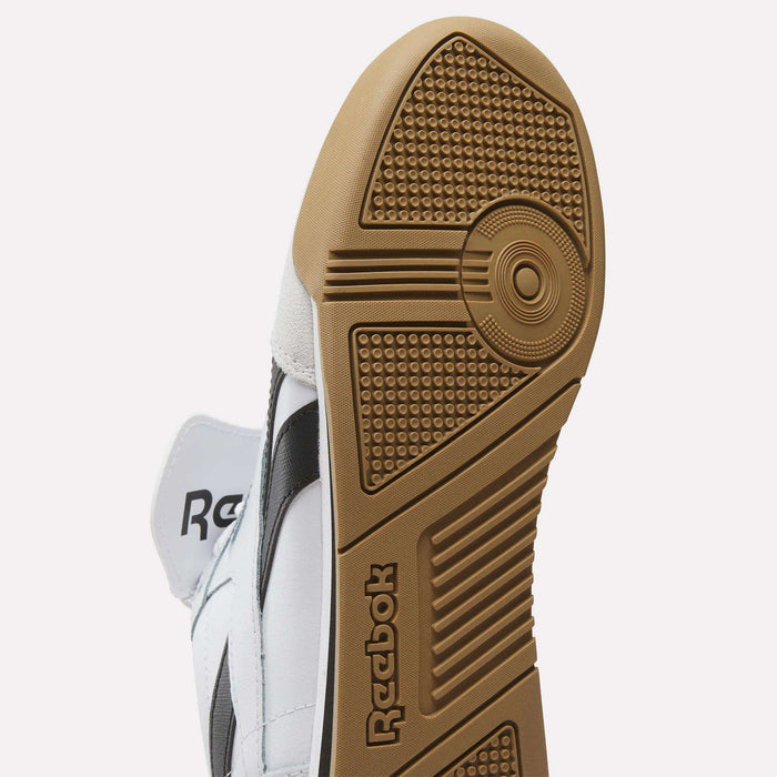 Close-up of the sole of Reebok Campio XT Kilty Shoes, featuring a brown rubber outsole with textured grip and embossed logo. The tennis-inspired design stands out with a white upper and black side stripe.