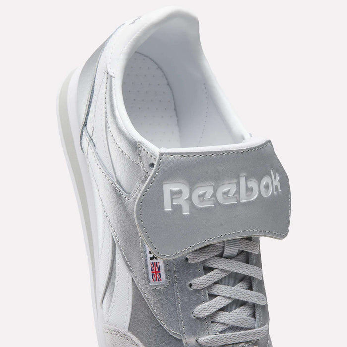 Close-up of Reebok Campio XT Kilty Shoes in gray and white with white laces, embossed Reebok logo on the tongue, and a small Union Jack label on the side, highlighting their classic tennis-inspired style.