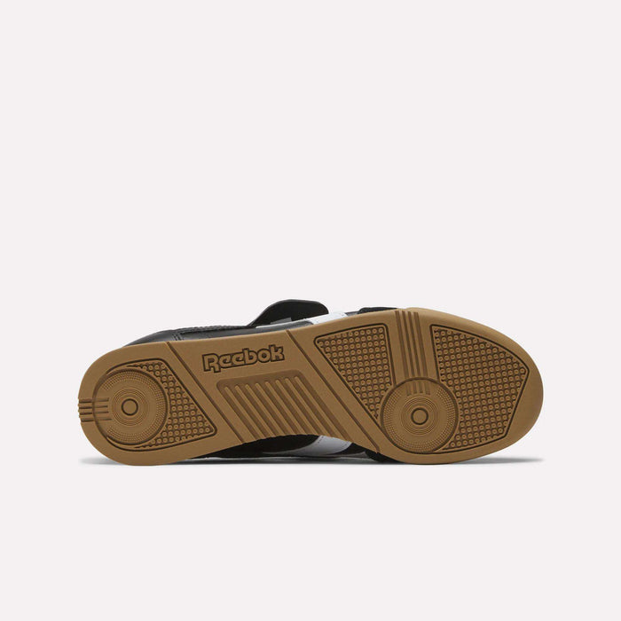The image displays the sole of a black Reebok Campio XT Kilty Shoe with a gum-colored bottom, featuring tennis-inspired style, a textured grip pattern, and an embossed Reebok logo that blend function and fashion.