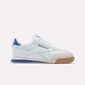 The Reebok Campio XT Shoes for Big Kids feature a white design with light blue and aqua accents, a gum sole, suede toe detail, and blue heel. Shown in side profile on a plain white background—ideal for stylish juniors' soccer shoes.