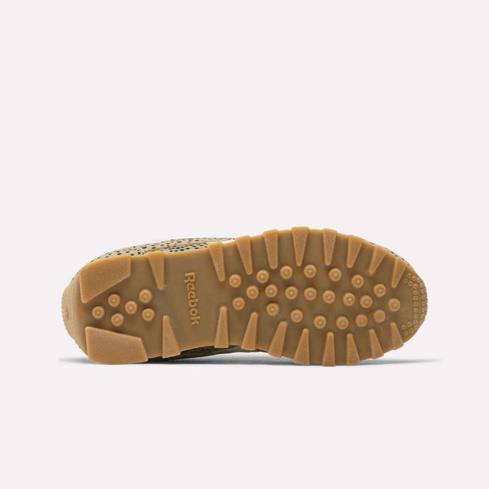 The image shows the sole of Reebok's Classic AZ Shoes - Little Kids, featuring a brown rubber outsole with textured grip patterns, the Reebok logo in the center, and circular and rectangular treads for traction.