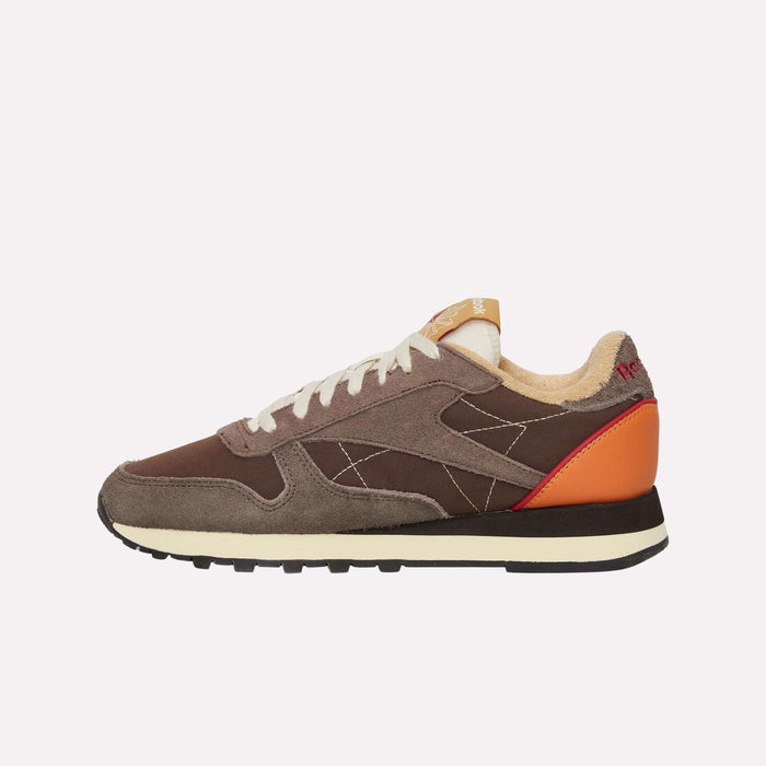 A brown and gray Reebok Classic Leather Premium LTD Shoe with white laces, orange heel detail, beige inner lining, and a black sole is displayed in profile against a plain white background—this retro sneaker from Reebok showcases a timeless, classic silhouette.