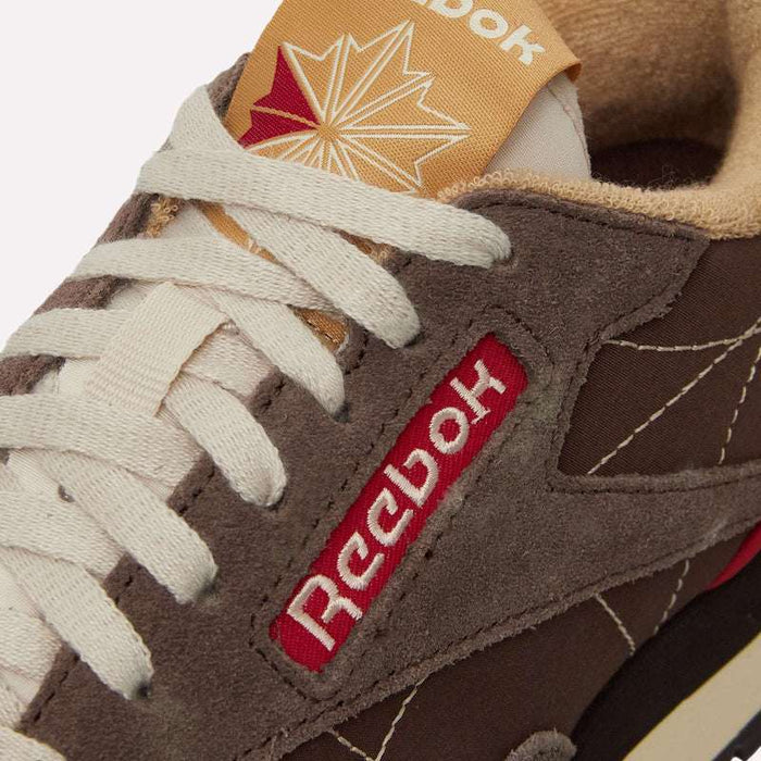 Close-up of a brown Reebok Classic Leather Premium LTD Shoe featuring white laces, red and white Reebok branding, and a maple leaf design on the beige tongue—all highlighting its classic silhouette.