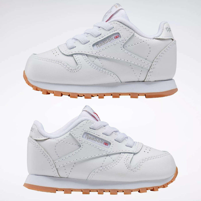 The Reebok Kids' Classic Leather Shoes - Baby & Toddler are white with white laces, light brown rubber soles, and display the iconic Reebok logo with a small UK flag on the side.