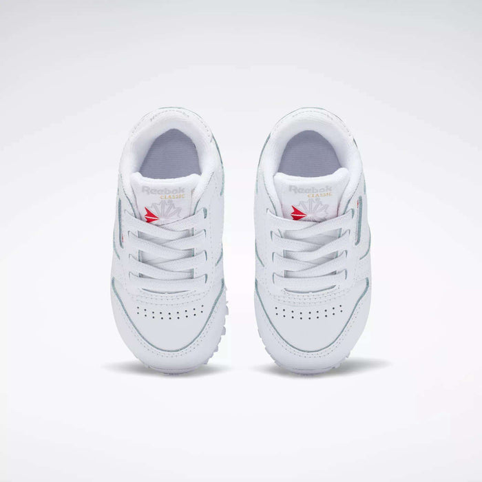 A pair of Kids' Classic Leather Shoes - Baby & Toddler by Reebok in white, featuring laces, toe perforations, and a red Reebok logo on the tongue, shown from above on a plain light background—ideal for toddlers’ everyday style.