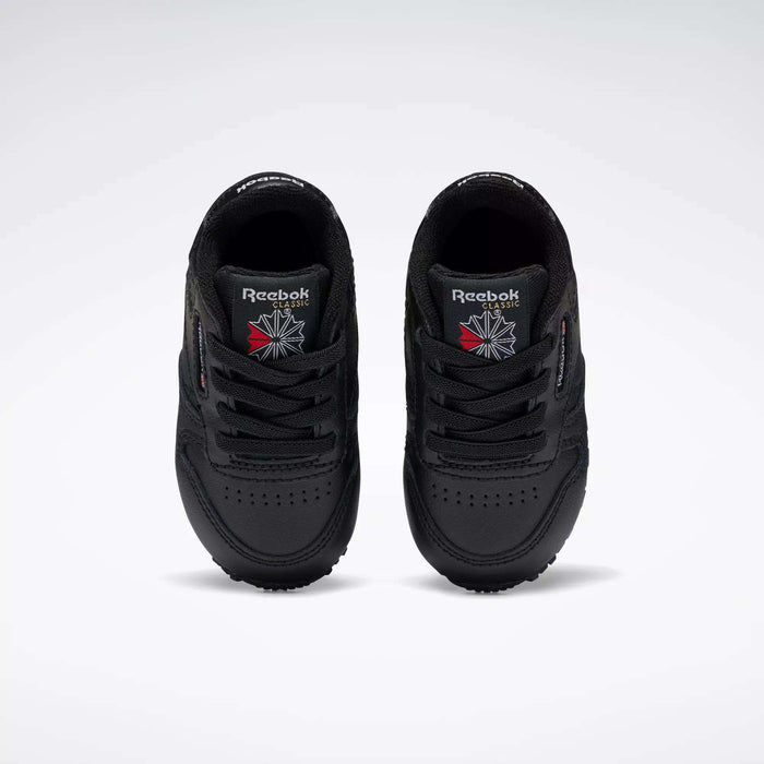 A pair of Reebok Kids' Classic Leather Shoes for baby & toddler in black, viewed from above with the Reebok logo and a red and white emblem on the tongues, set against a plain white background—ideal for young fans of classic sneakers.