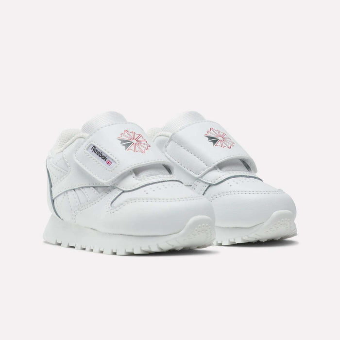 The Reebok Kids' Classic Leather Shoes are white toddler sneakers with Velcro straps, pink Reebok logos on the sides and tongues, and textured white soles—ideal for casual everyday wear, shown on a plain white background.