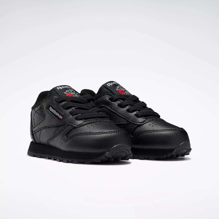 A pair of Kids' Classic Leather Shoes - Baby & Toddler by Reebok, in black leather with black laces, detailed stitching, and Reebok logos on the side and tongue, displayed on a plain white background.
