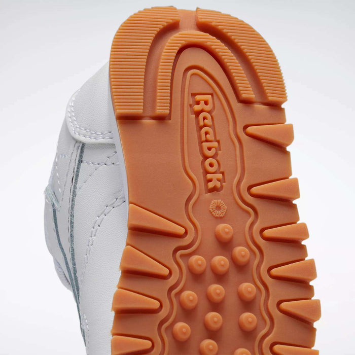 Close-up of the orange sole on Reebok Kids' Classic Leather Shoes—Baby & Toddler—with brand name, textured tread, and part of the white upper with gray accents visible.