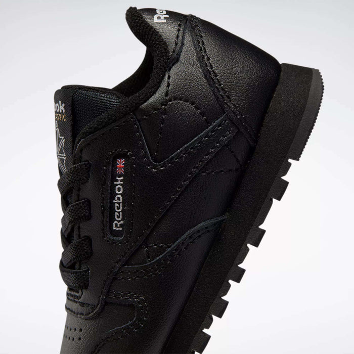 Close-up of Kids' Classic Leather Shoes by Reebok for babies and toddlers, featuring a black design with visible logo, black laces, and rugged sole, showcasing retro sneaker style against a plain white background.