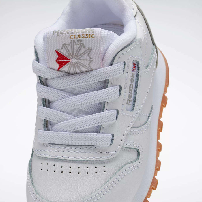 Close-up of Reebok Kids' Classic Leather Shoes - Baby & Toddler, featuring white leather, logo on tongue, laces, perforated toe, stitched details, and a gum outsole—ideal for toddler style and comfort.