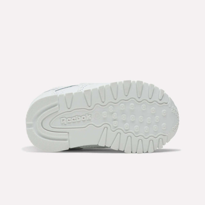 The image shows the sole of Reebok Kids' Classic Leather Shoes in white, featuring textured tread patterns and a central Reebok logo. These casual sneakers are perfect for everyday wear and are photographed against a plain, light-colored background.