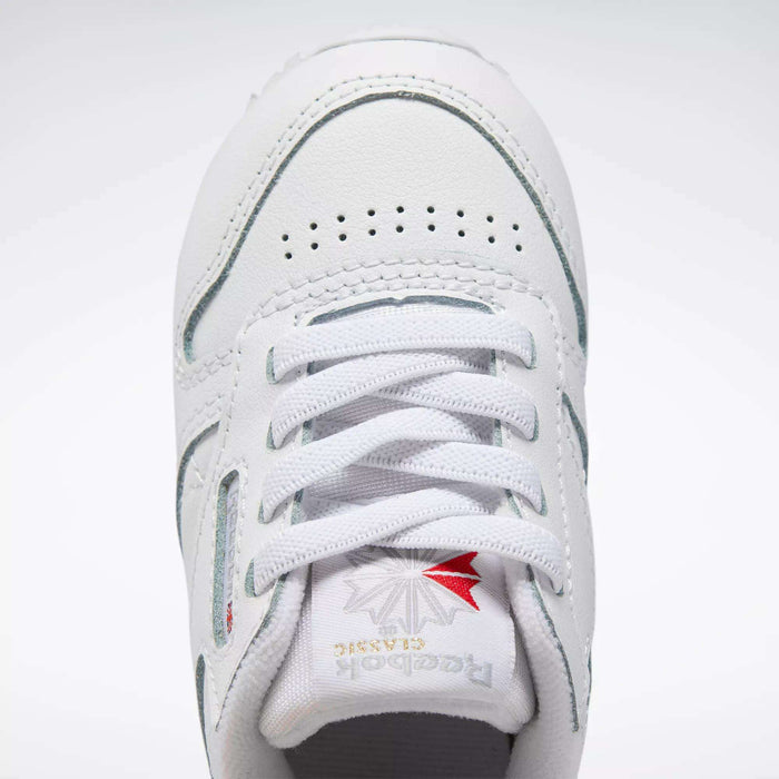 Close-up of Kids' Classic Leather Shoes - Baby & Toddler by Reebok, featuring white leather, laces, perforated toe box, and tongue with silver and red Reebok branding—ideal for active toddlers.