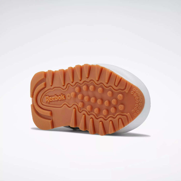The image shows the sole of a Reebok Kids' Classic Leather Shoe for babies and toddlers, featuring a gum rubber outsole with textured tread and the Reebok logo near the heel. The shoe is displayed sole-up against a plain background.