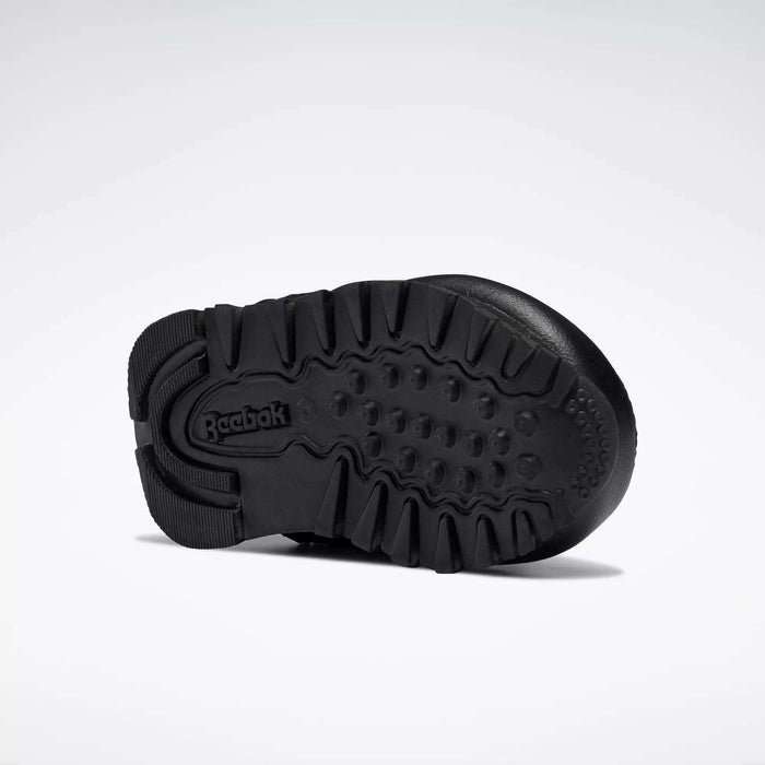 The image displays the black rubber sole of Reebok Kids' Classic Leather Shoes for babies and toddlers, featuring deep treads and the Reebok logo at the heel, set against a plain white background—ideal for young fans of classic sneakers.