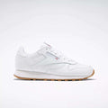 A Reebok Classic Leather Shoes - Big Kids sneaker in white with a gum sole, stitched side-stripe, side logo, and red, white, and blue Reebok emblem is shown from the side against a plain light background.