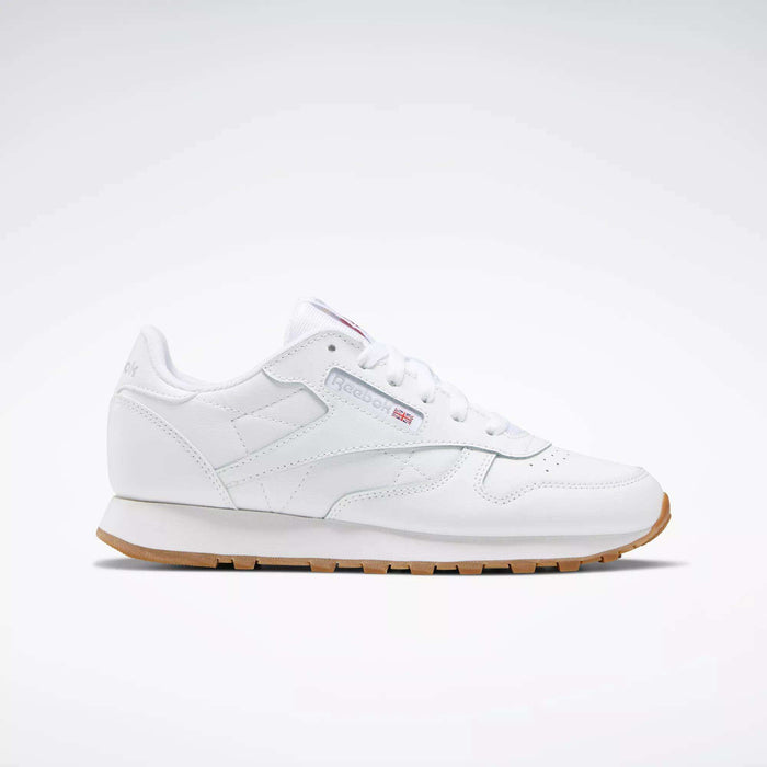 A Reebok Classic Leather Shoes - Big Kids sneaker in white with a gum sole, stitched side-stripe, side logo, and red, white, and blue Reebok emblem is shown from the side against a plain light background.