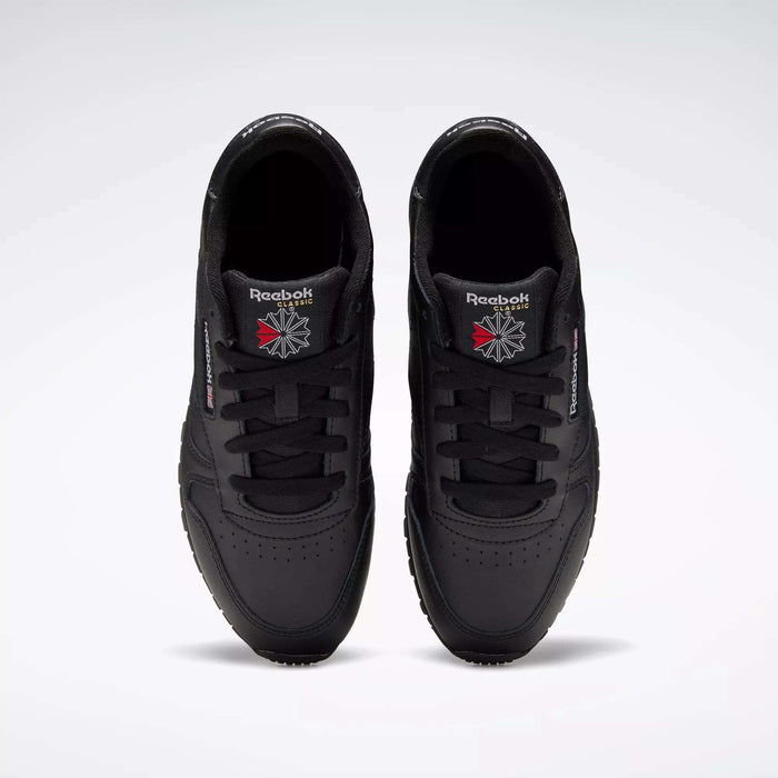 A pair of Reebok Classic Leather Shoes - Big Kids is seen from above, displaying the black uppers and logos on the tongues against a plain light gray background.