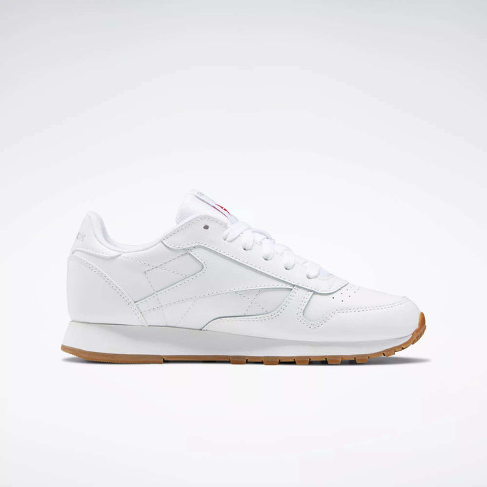 The Reebok Classic Leather Shoes - Big Kids feature a white leather upper, classic stitched side-stripe, white laces and sole, plus a light brown rubber outsole. Shown in side profile against a plain background. Ideal for junior boys' shoe collections.