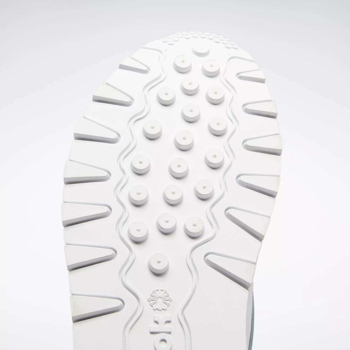 Close-up of a white sole from the Reebok Classic Leather Shoes - Big Kids, featuring round raised bumps and wavy grooves for traction. The classic design stands out against a light gray background, ideal for junior boys.