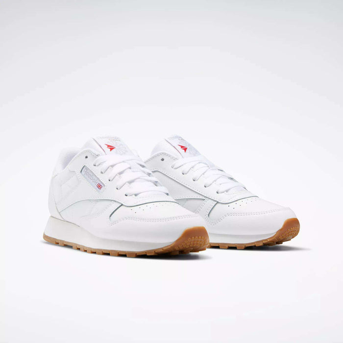 A pair of Reebok Classic Leather Shoes - Big Kids, in white with stitched side-stripe, gum rubber soles, subtle branding, and white laces are placed side by side on a plain white background.
