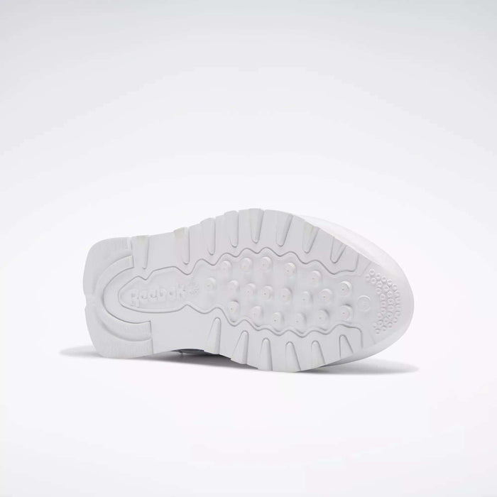 The image displays the white rubber outsole of Reebok Classic Leather Shoes for Big Kids, showing textured grip patterns and the embossed Reebok logo near the heel. The shoe is positioned on its side against a plain, light background.