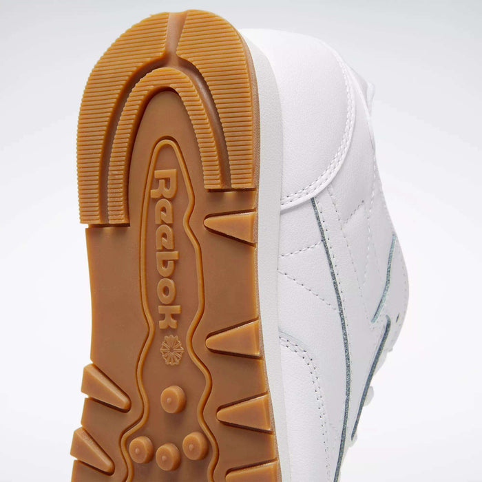 Close-up of the sole of Reebok Classic Leather Shoes - Big Kids, featuring a tan rubber outsole with logo and textured grip. The white upper has classic stitched side-stripes—ideal for junior boys' shoe collections.