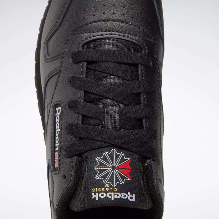 Close-up, top-down view of black Reebok Classic Leather Shoes for big kids, featuring black laces, perforated toe box, and the iconic Union Jack and starburst Reebok logo on the tongue—ideal for boys’ shoe collections.