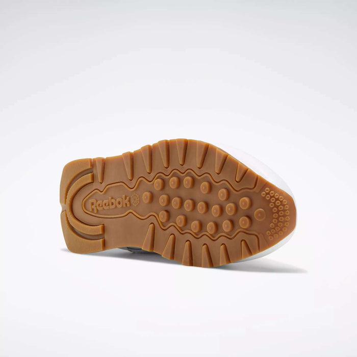The image shows the bottom view of Reebok Classic Leather Shoes - Big Kids, featuring a textured light brown rubber sole with varied patterns and the embossed Reebok logo near the heel.
